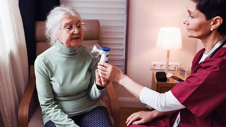 A healthcare worker helps a lady to use a nebuliser.
