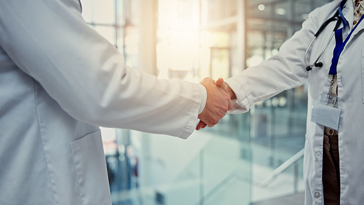 Two people shaking hands in a clinical setting with a bright background.