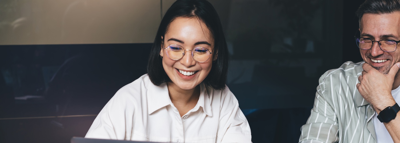 A young woman at a laptop with a man sitting next to her. Both are smiling.