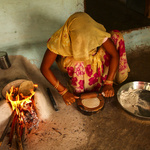An Asian woman rolling out chapatis next to a cooking fire.