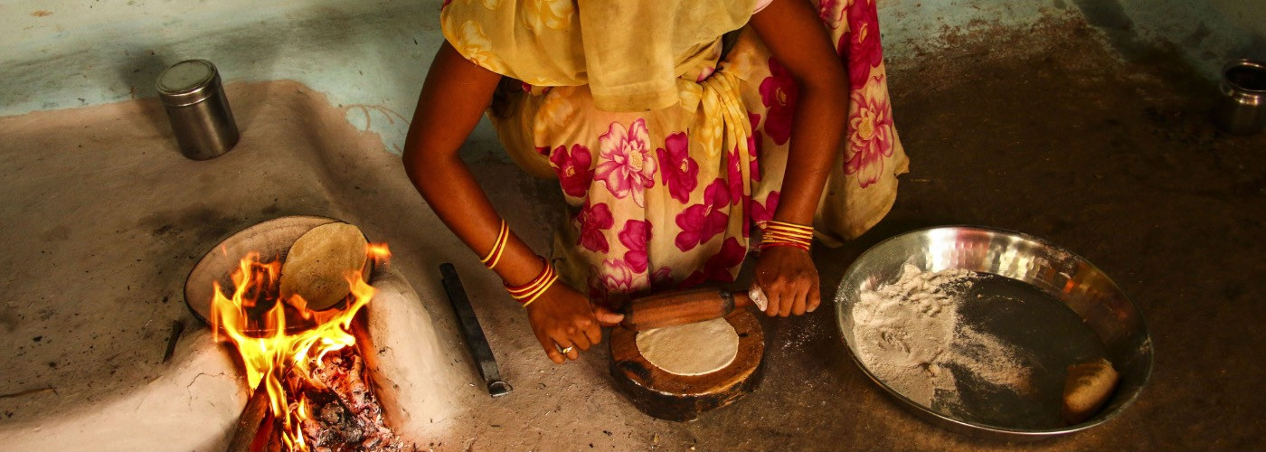 An Asian woman rolling out chapatis next to a cooking fire.