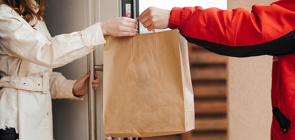 A food delivery driver handing a paper bag to a customer at the door.