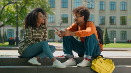 Two Black people sitting on steps and talking.