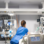 A clinician on a medical ward tending to a bed surrounded by medical equipment and machines.