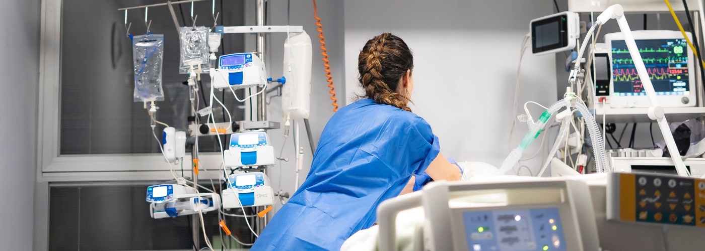 A clinician in a blue uniform, tending to a patient in a hospital ward.