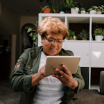 An older Black woman using an iPad at home.