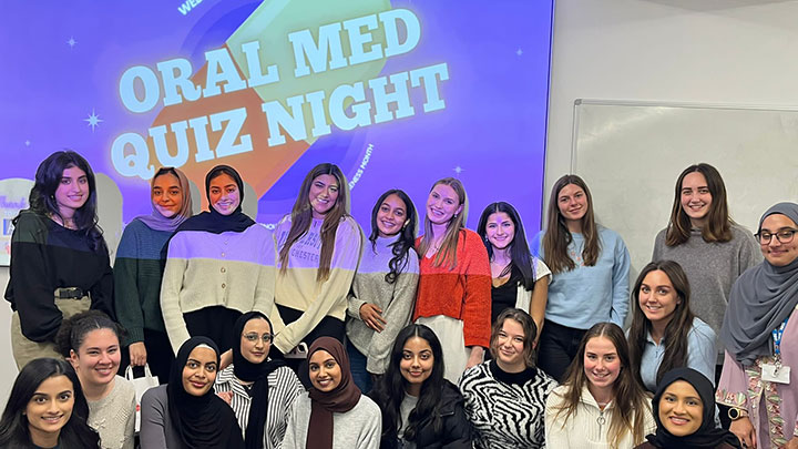 A group of dental students standing in front of a projected screen with 'oral med quiz night' on it.