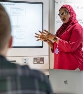 A female postgraduate researcher stands at an interactive whiteboard presenting