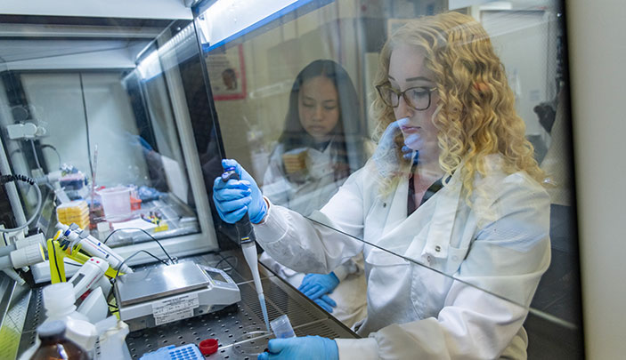 A postgraduate researcher in a white lab coat using a pipette.