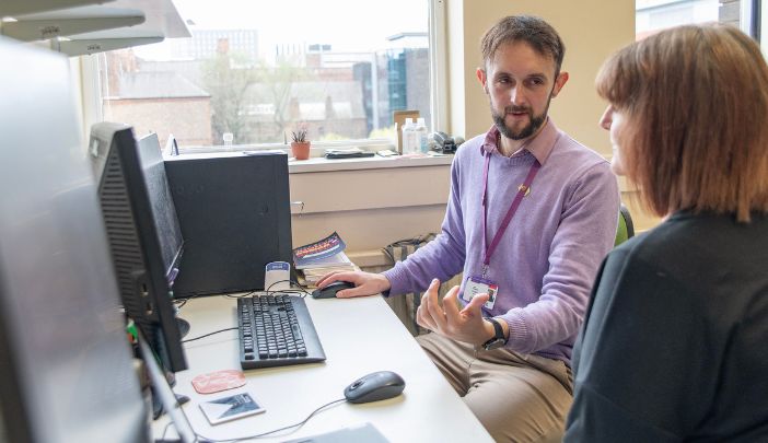 A postgraduate researcher sat talking with an academic in front of their laptop 