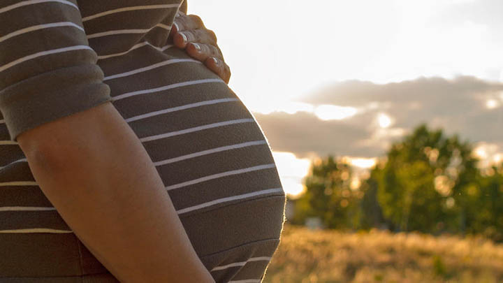 A pregnant woman standing outside in a nature setting.