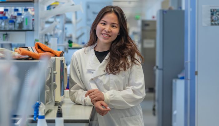 A female researcher in a lab coat smiling looking at the camera