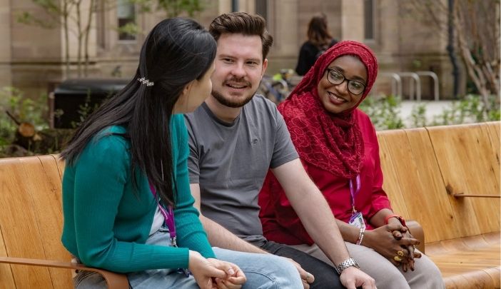 Three postgraduate researchers sat at a bench chatting