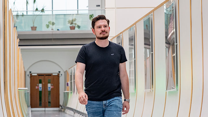 Connor, a postgraduate research student, standing on bridge between two campus buildings.