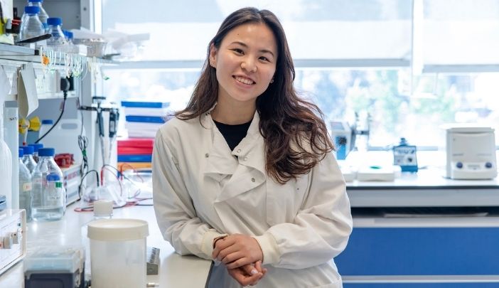 Female postgraduate researcher in lab coat looking at camera