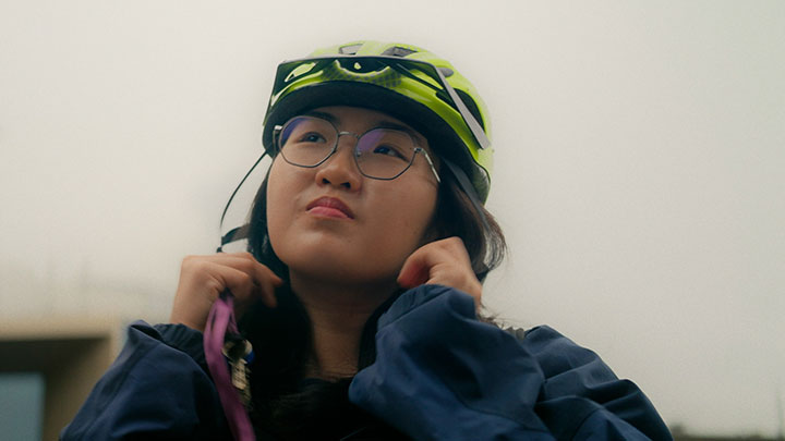 Candid photo of a woman putting on a bike helmet, looking into the distance.