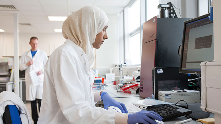 A woman sitting at a computer in a lab wearing a lab coat.