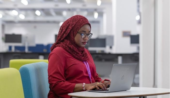 A postgraduate researcher sat in a library looking at a laptop