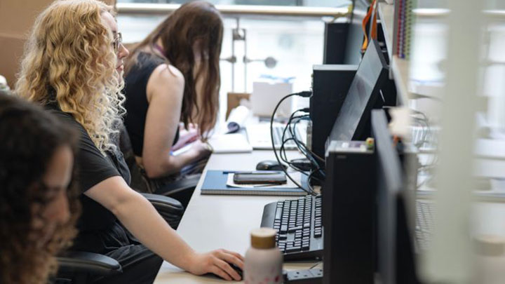 Postgraduate researcher Holly working on a computer in a busy computer lab.