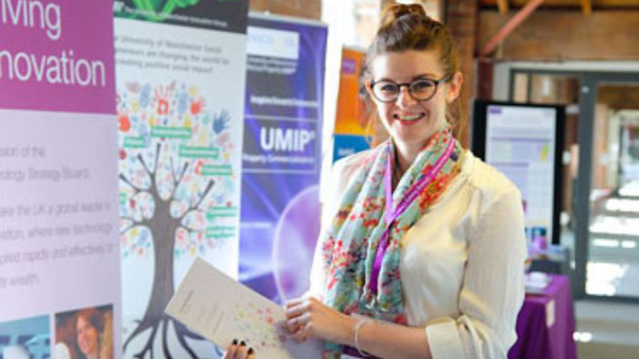 A postgraduate researcher holding a document and smiling at the camera.