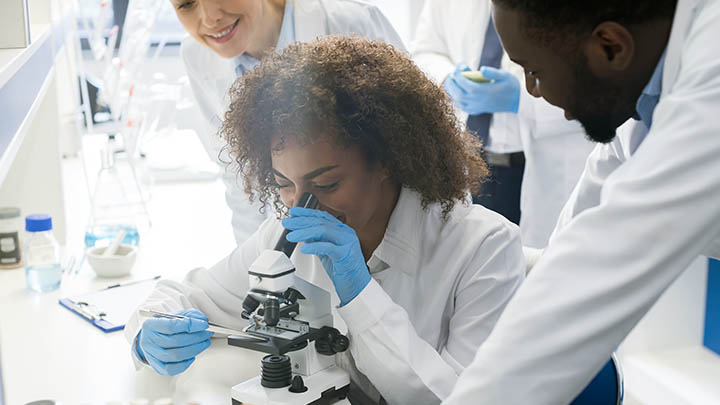 Students gathered around microscope in lab.